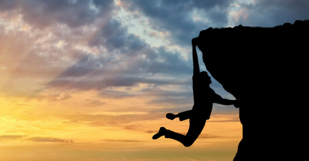 Man climbing a cliff at dusk - providing comprehensive benefits is a challenge.